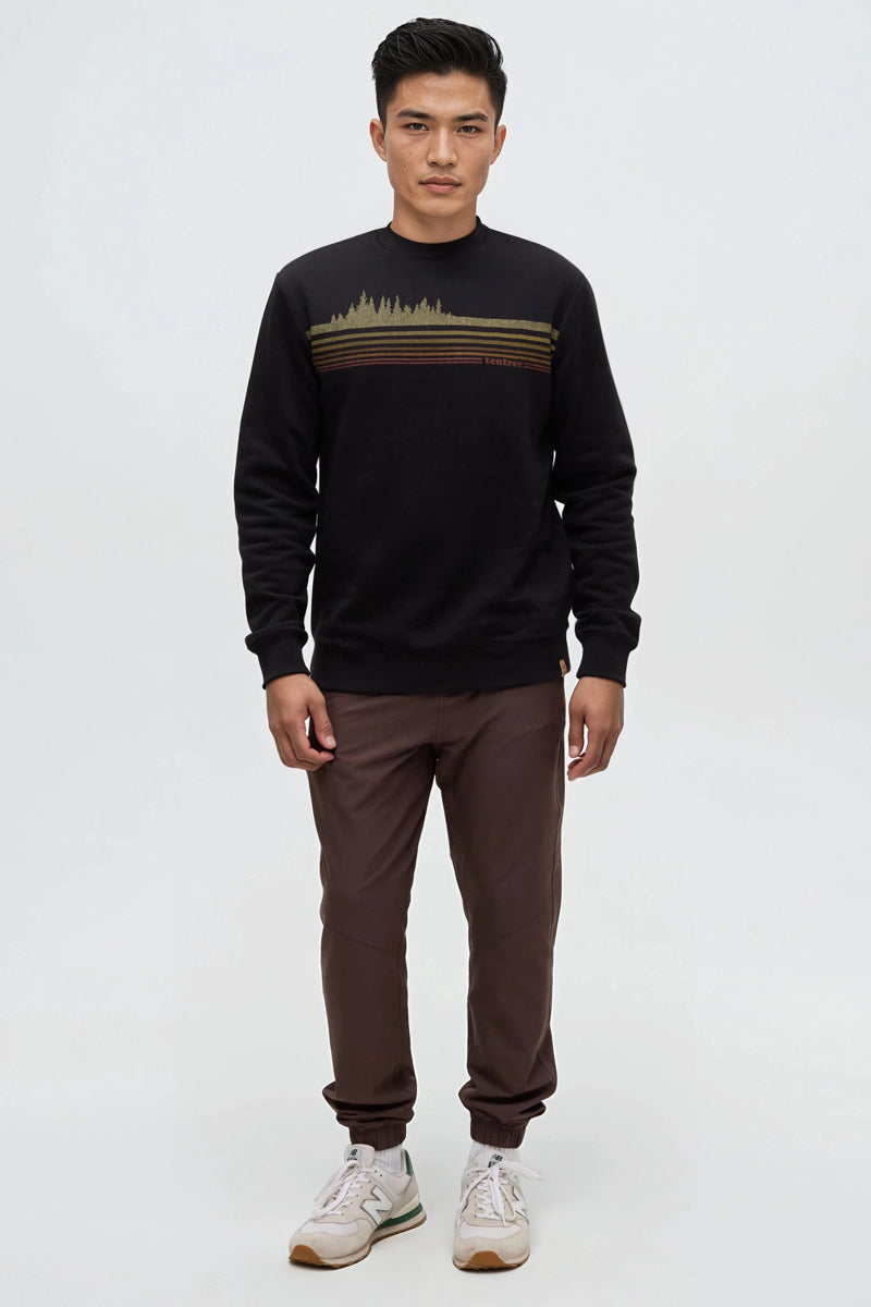 Man wearing a black sweater with a gold stripe and brown pants on a white background