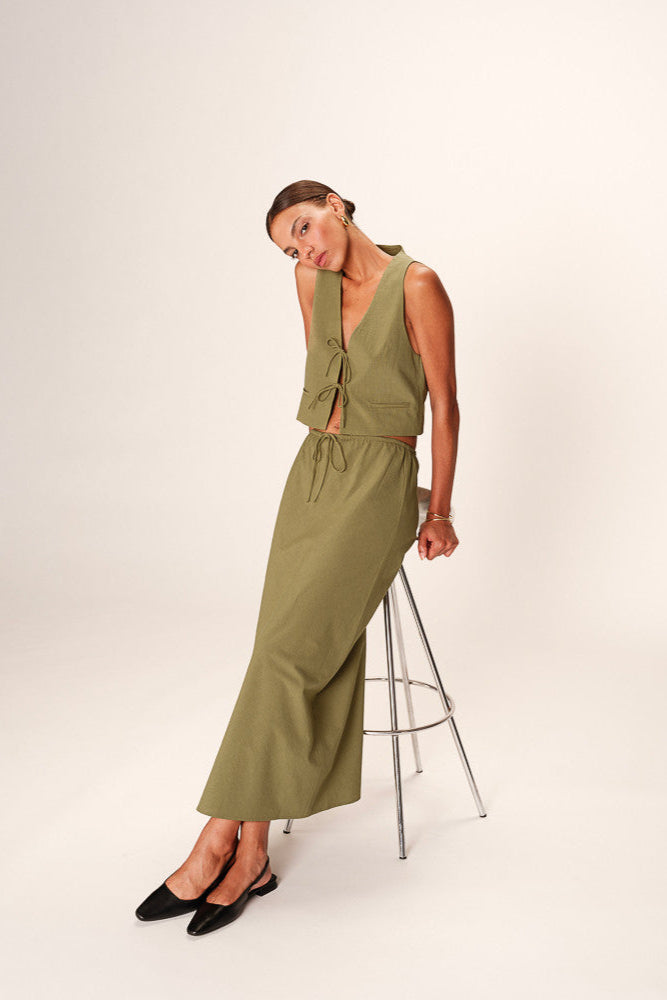 Woman wearing a green dress standing on a stool against a white background