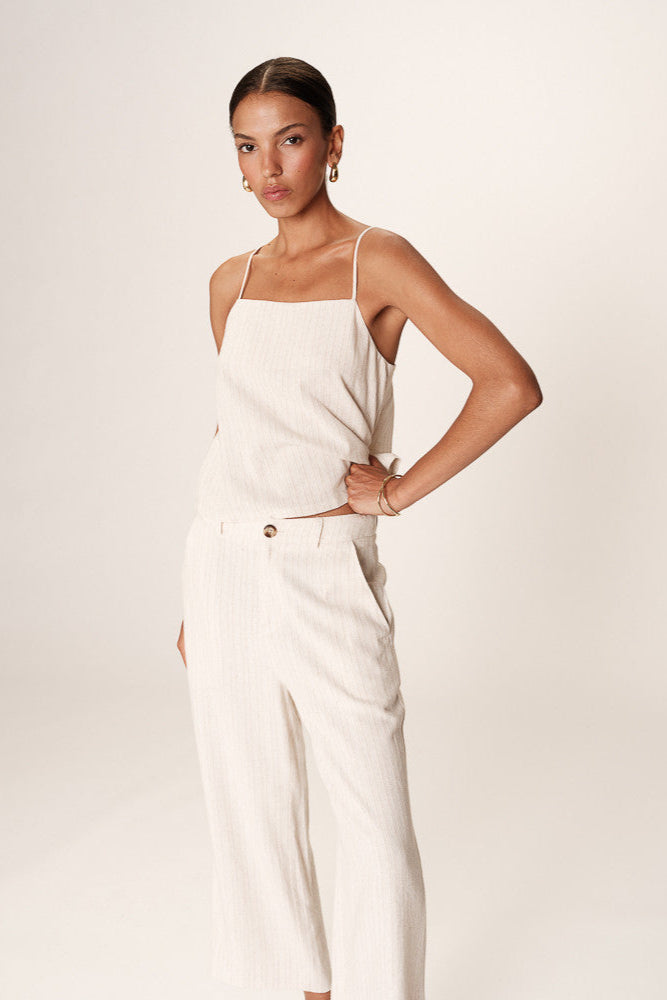 Woman wearing a white sleeveless top and pants against a plain background