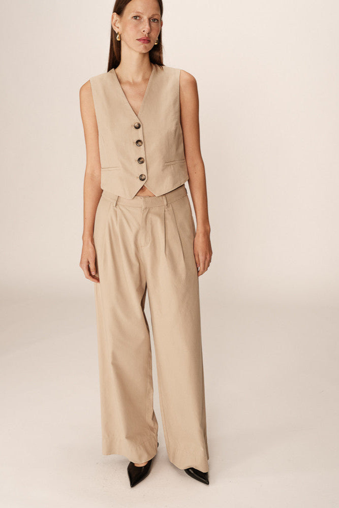 Woman wearing a beige vest and pants set on a plain background