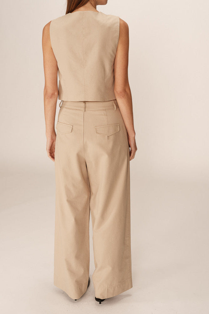 Person wearing a beige sleeveless top and wide-leg pants on a plain background