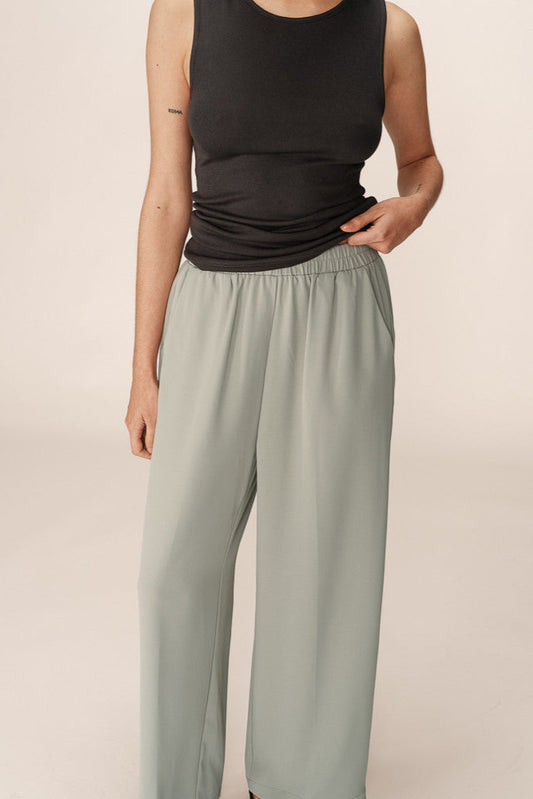 Person wearing a black sleeveless top and light gray pants on a beige background