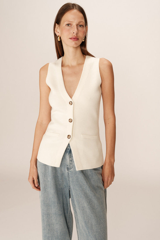 Woman wearing a cream-colored vest over a blue top on a plain background