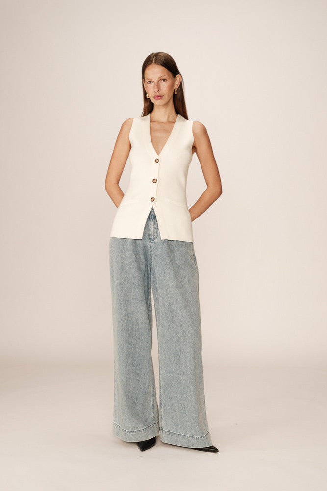 Woman wearing a cream vest and light blue jeans on a plain background