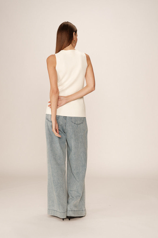 Woman wearing a white sleeveless top and light blue jeans on a plain background
