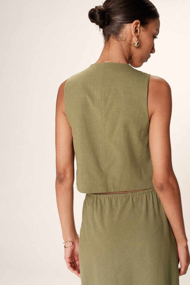 Woman wearing a green sleeveless top and skirt set on a plain background