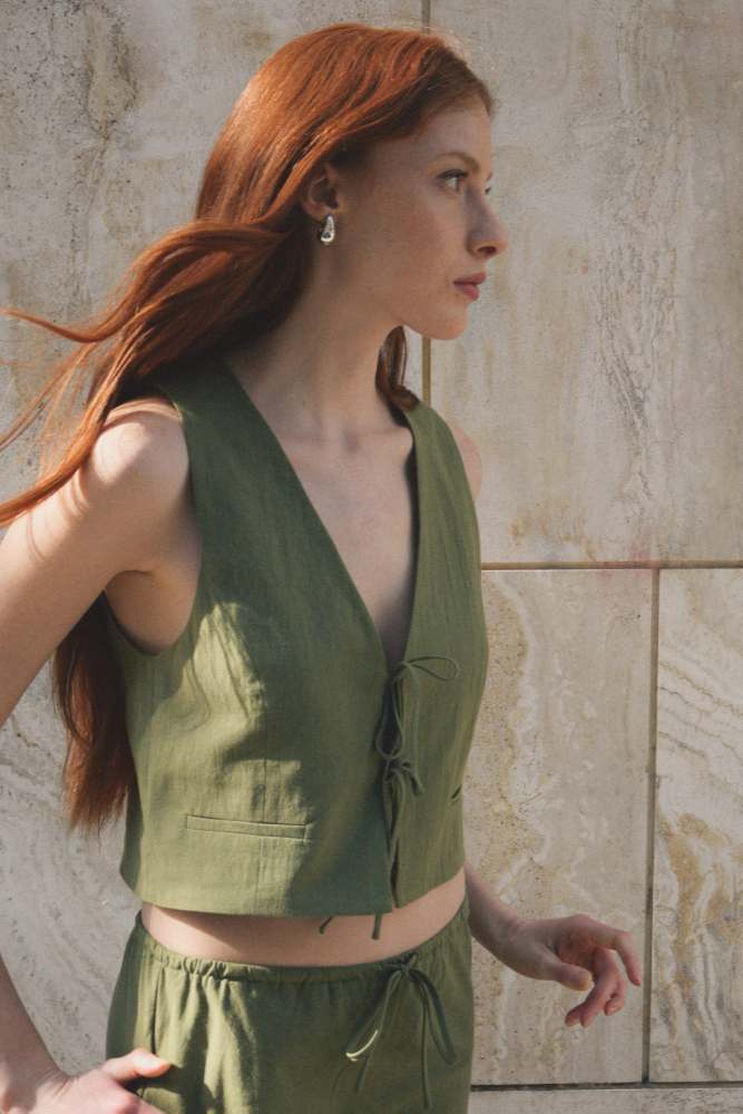 Woman wearing a green sleeveless top and pants against a stone wall.