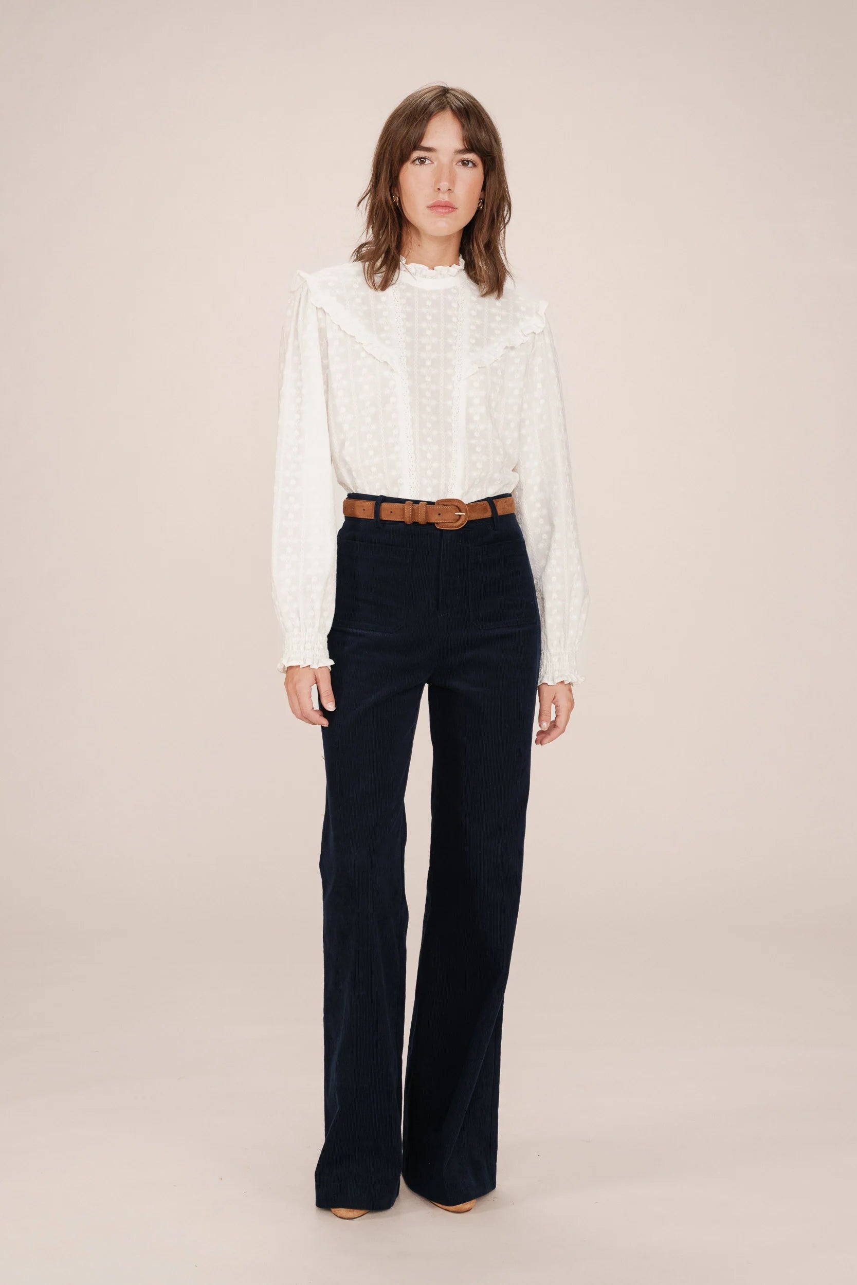 Woman wearing a white blouse and dark blue pants on a beige background