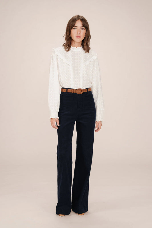 Woman wearing a white blouse and dark blue pants on a beige background