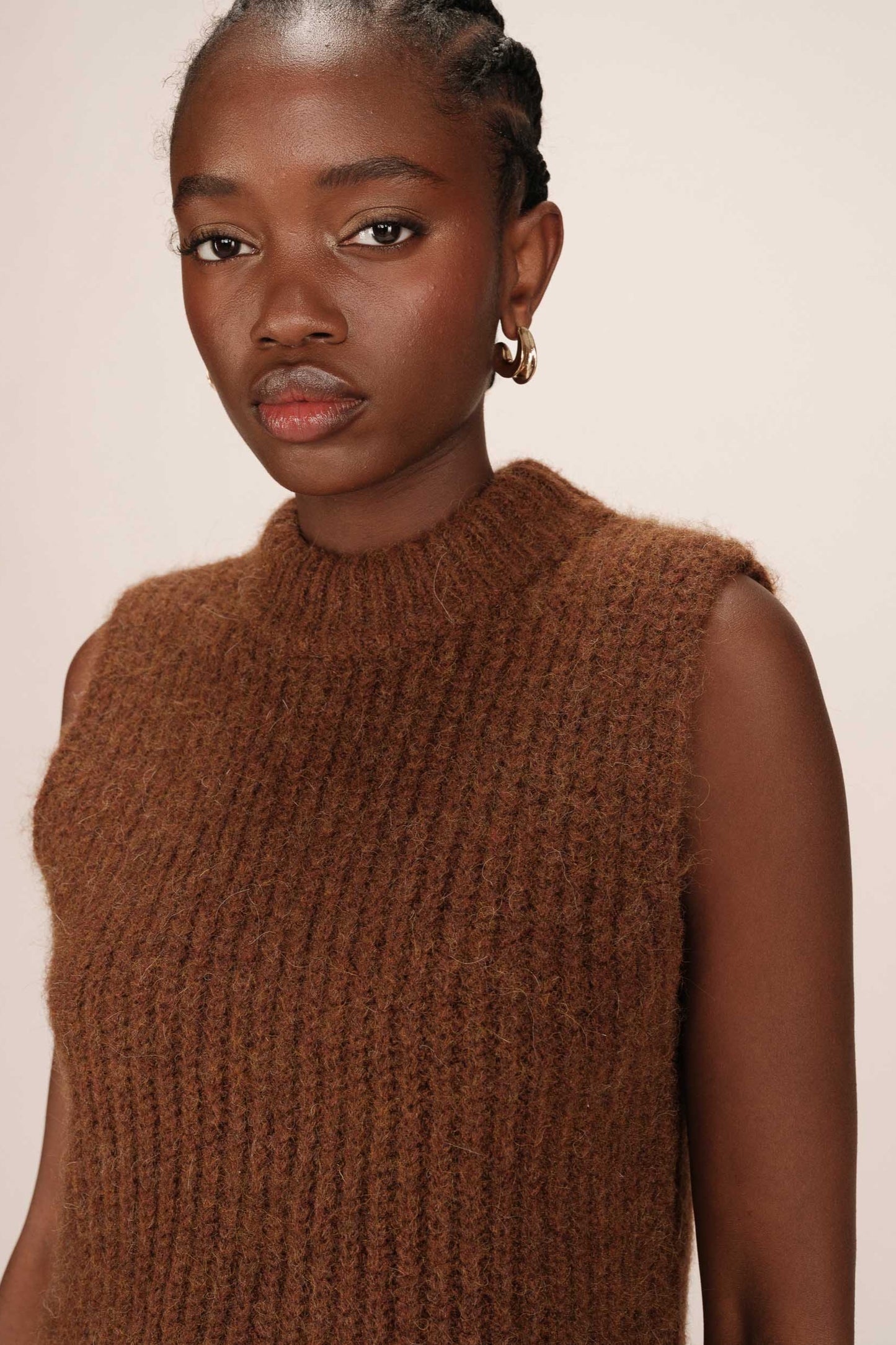 Woman wearing a brown knitted sleeveless sweater against a plain background