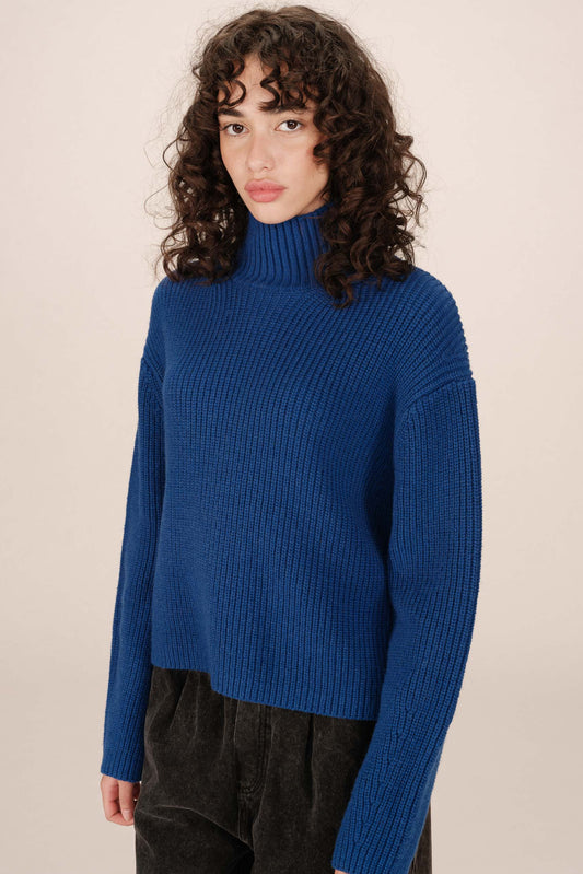 Woman wearing a blue turtleneck sweater against a beige background