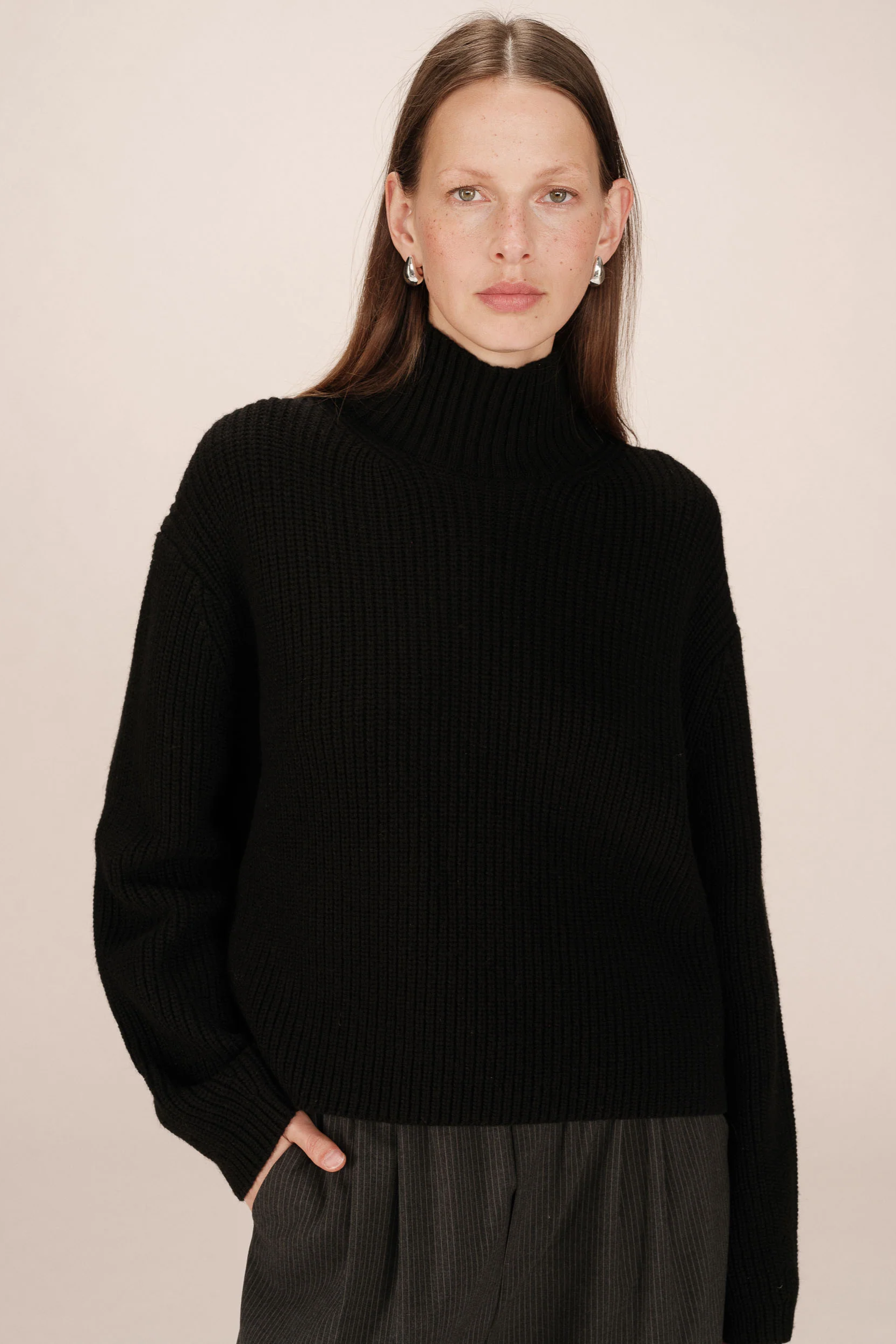 Woman wearing a black turtleneck sweater against a beige background