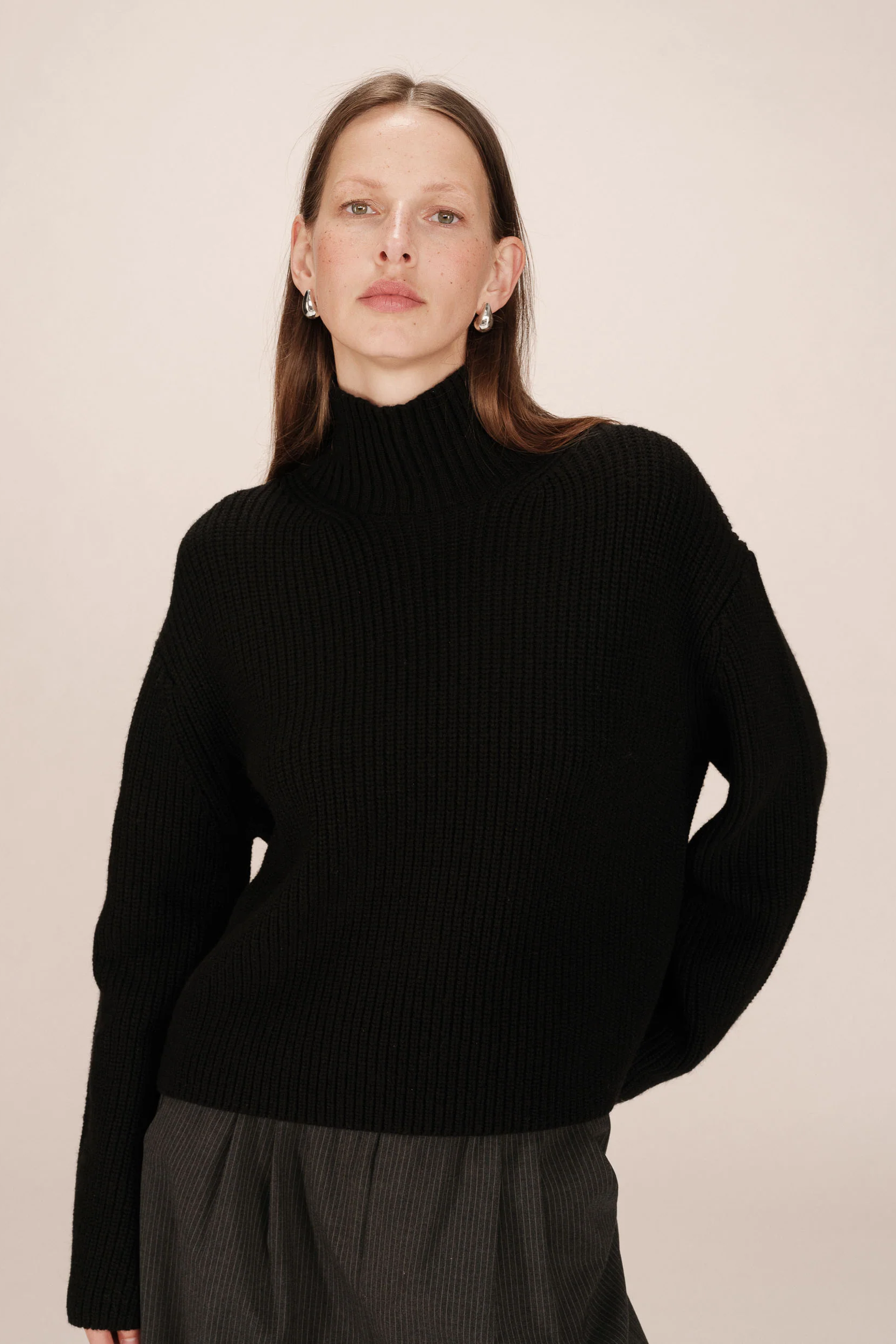 Person wearing a black turtleneck sweater against a beige background