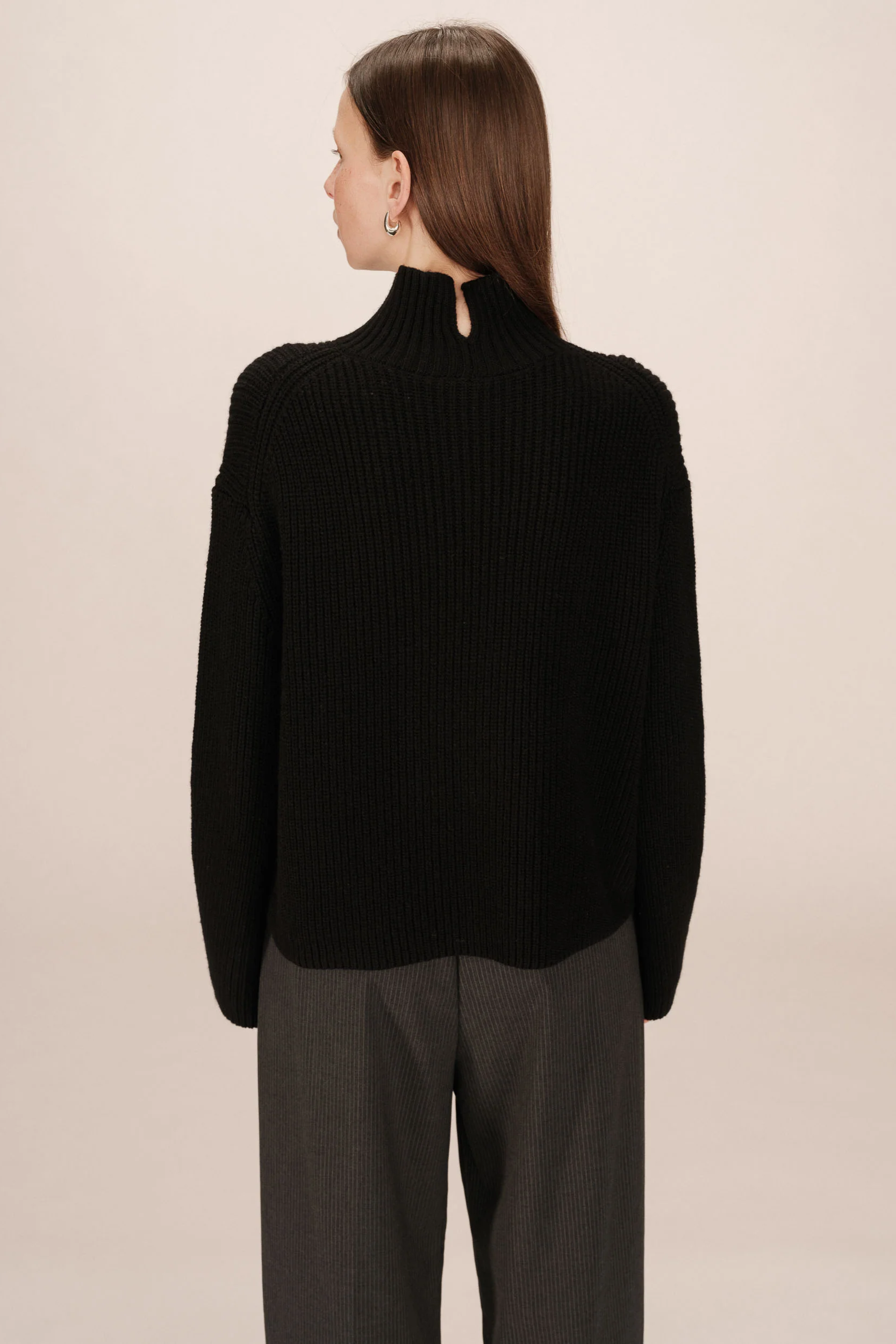 Person wearing a black sweater and gray pants on a beige background