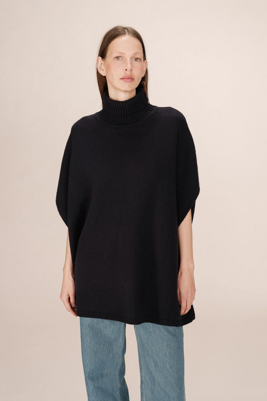 Person wearing a black turtleneck sweater and light blue jeans on a beige background