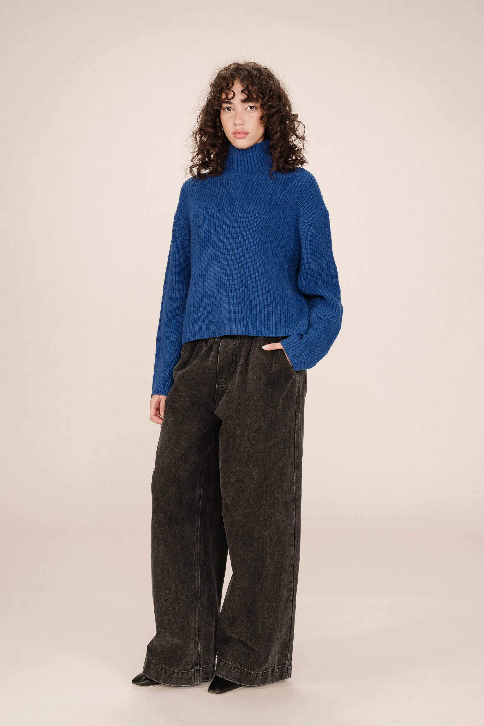 Person wearing a blue sweater and dark pants on a beige background