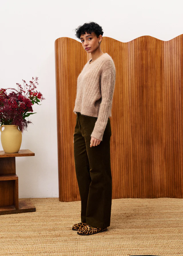 Woman standing in a room with wooden paneling and a vase of flowers.