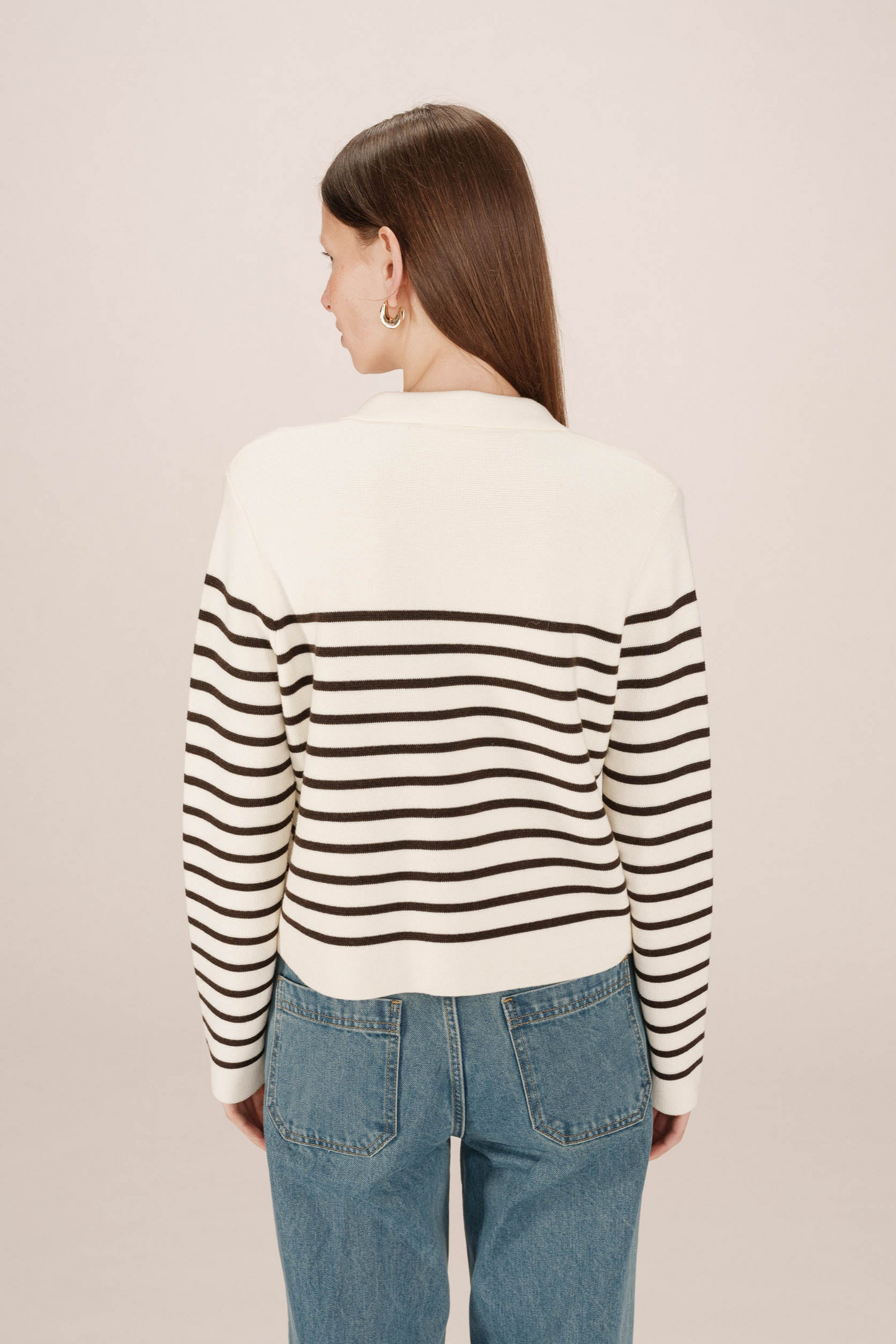 Person wearing a black and white striped sweater with blue jeans on a plain background