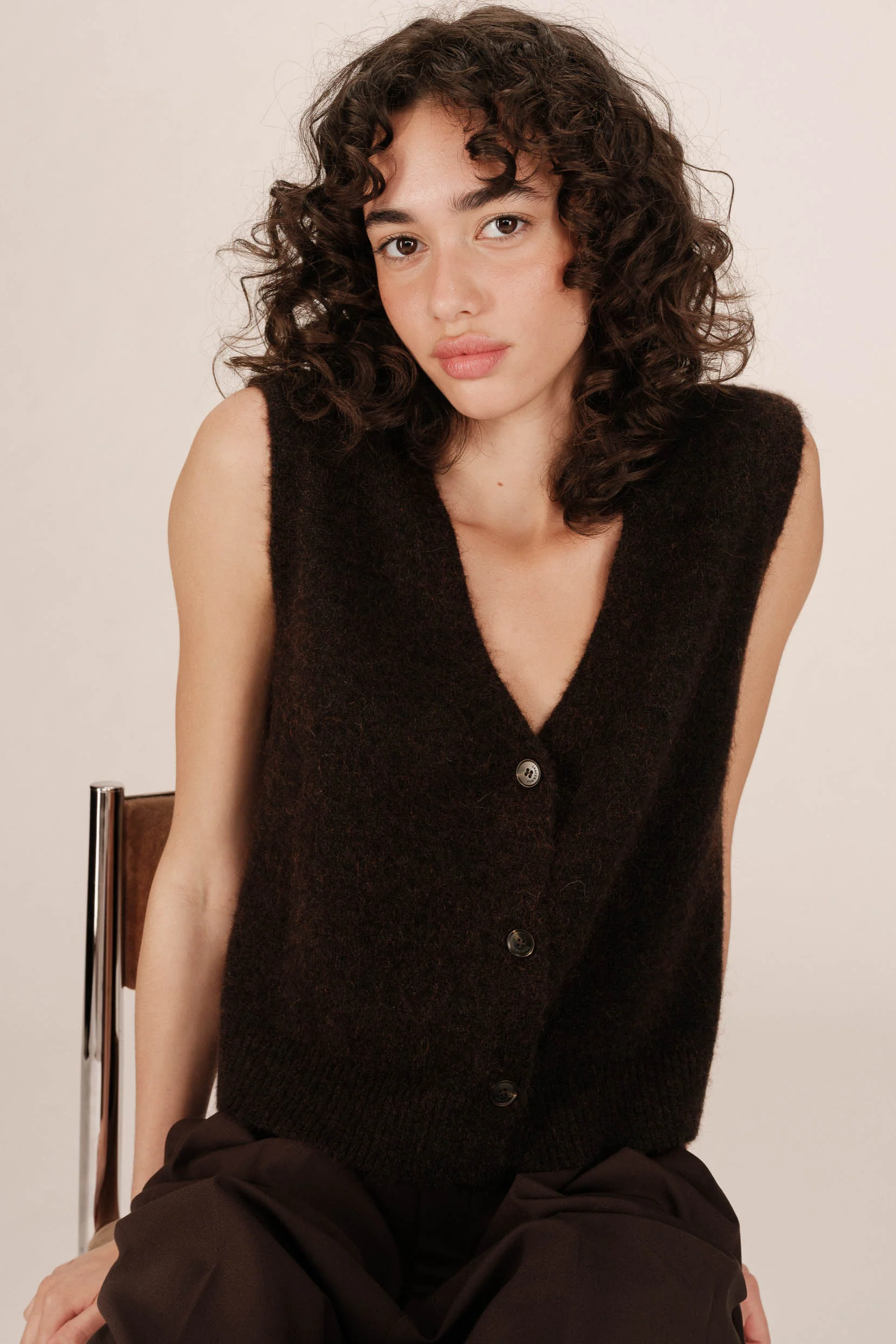 Woman wearing a black sleeveless sweater against a plain background
