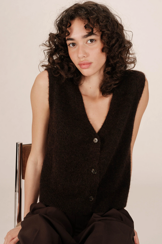 Woman wearing a black sleeveless sweater against a plain background