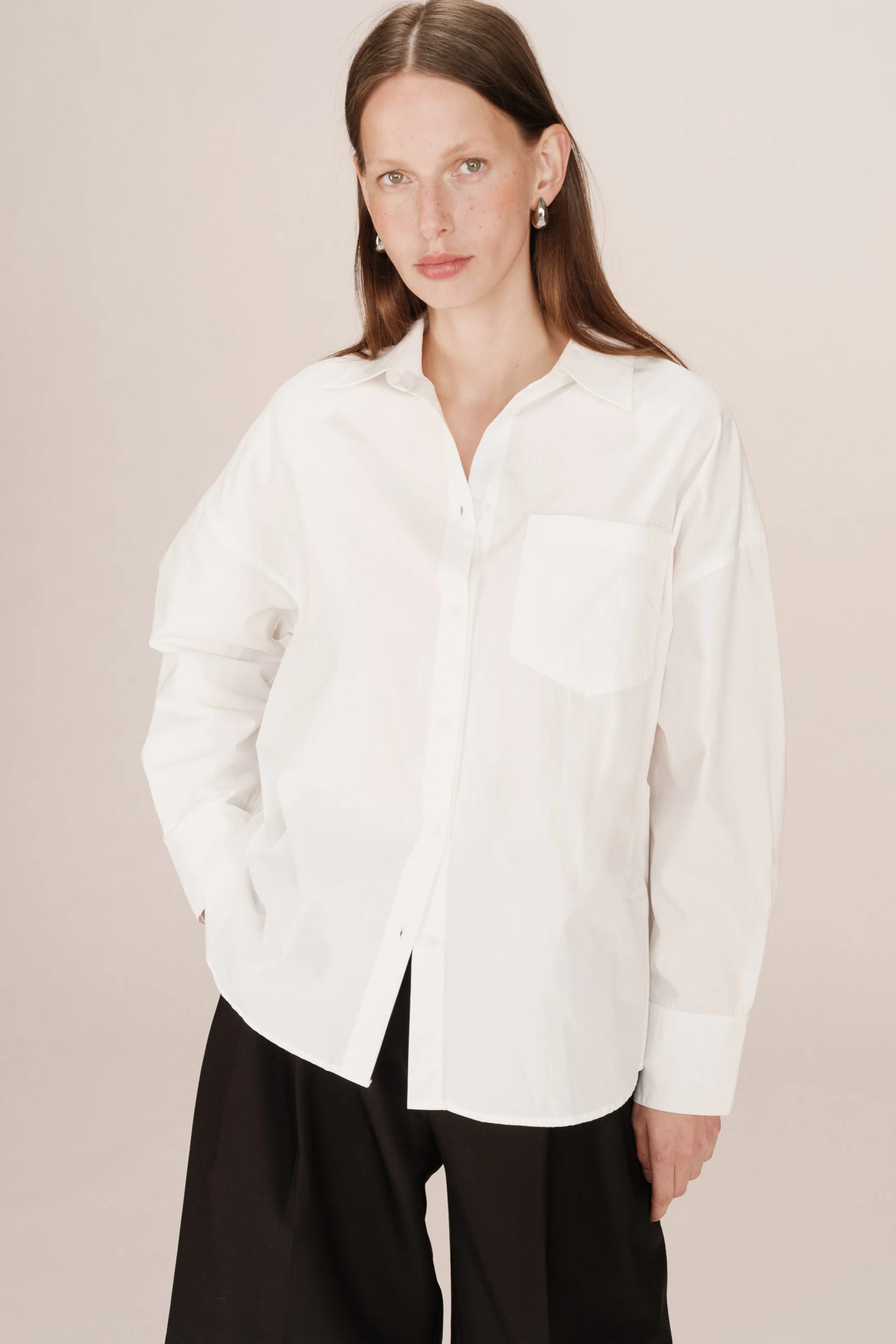 Woman wearing a white shirt and black pants against a plain background