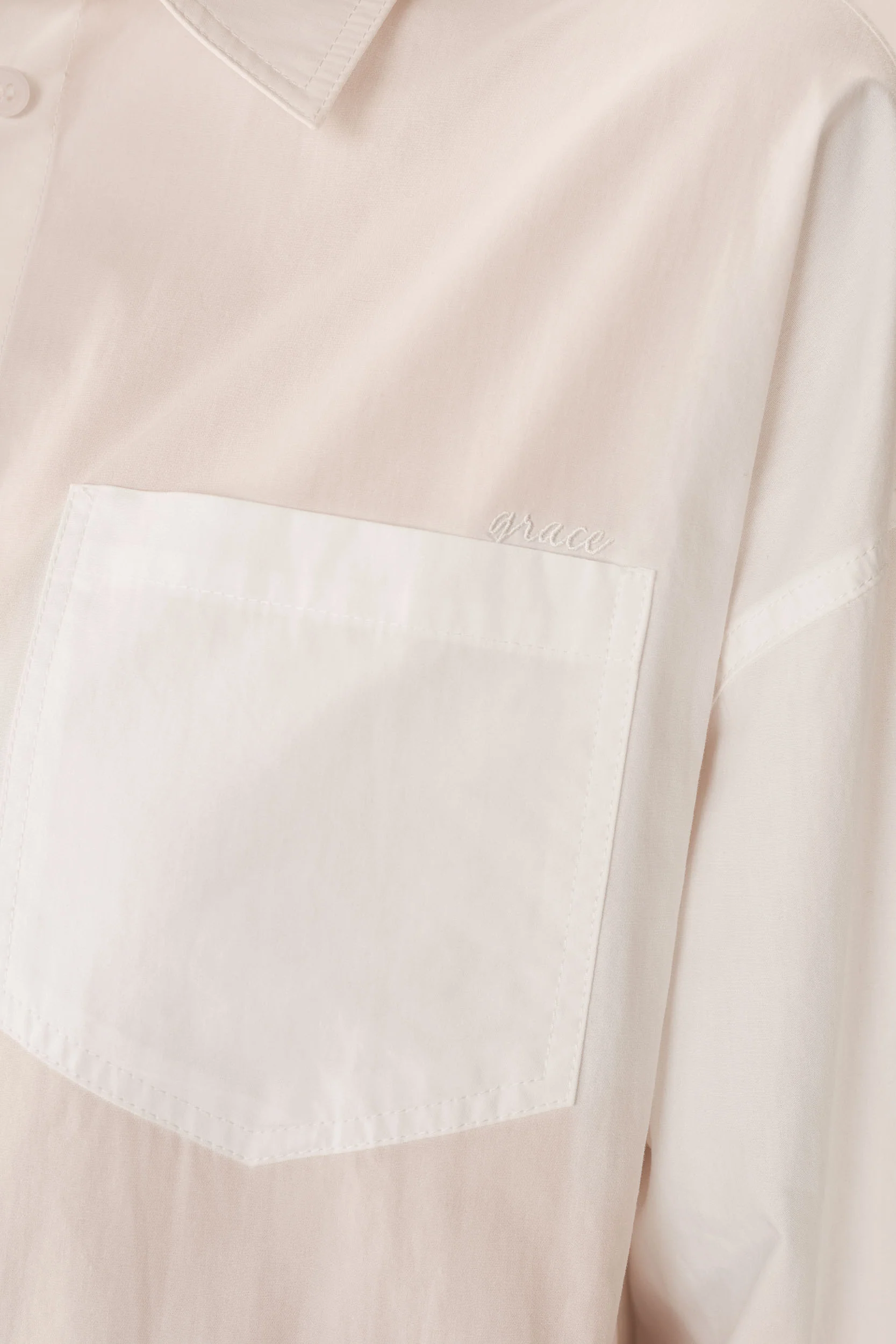 Close-up of a light pink shirt with a white pocket detail.