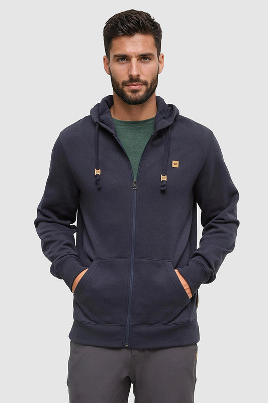 Man wearing a navy blue hoodie with brand logos on a light gray background