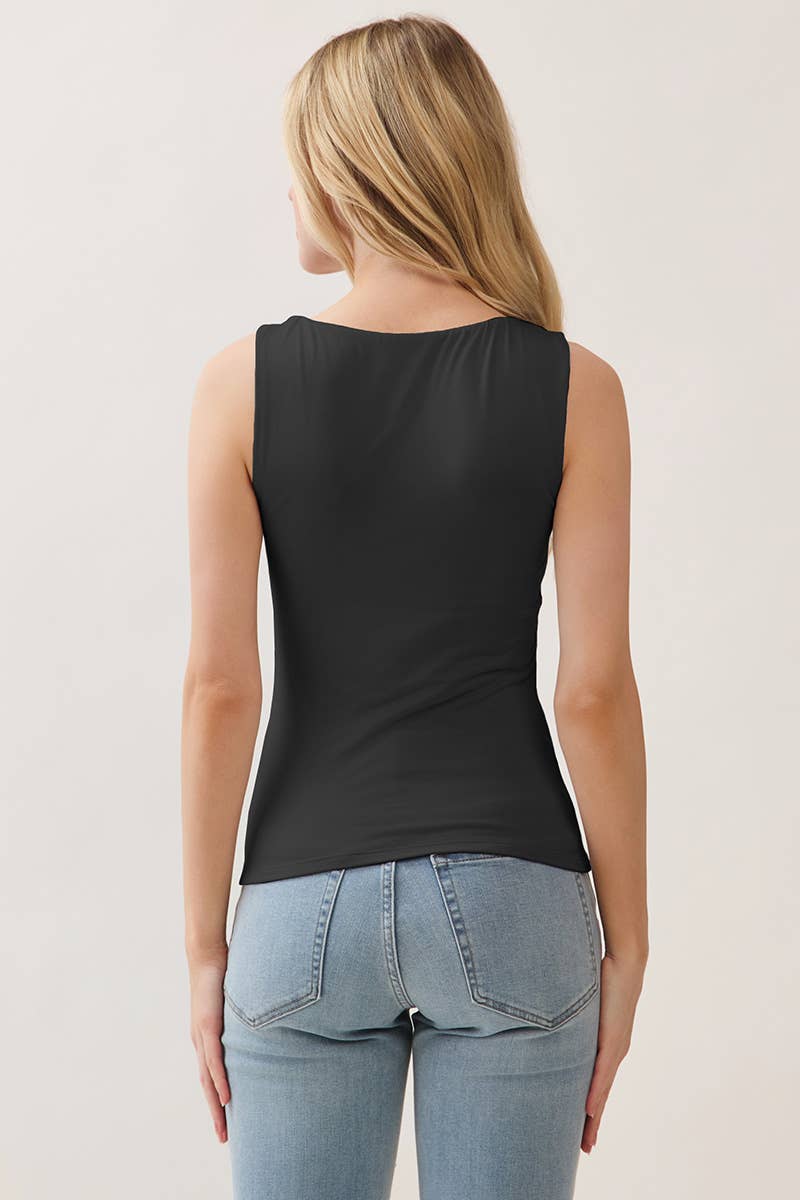 Woman wearing a black sleeveless top and blue jeans against a plain background