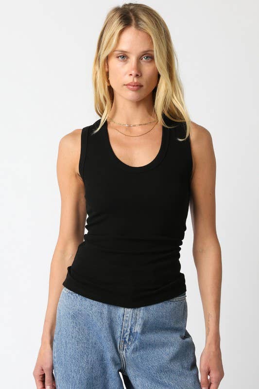 A blonde model wearing a black scoop-neck tank top and light-wash blue jeans, standing against a plain light gray studio background.