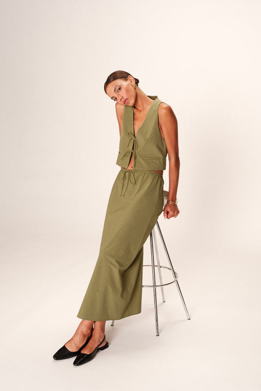 Woman wearing a green dress standing on a stool against a white background