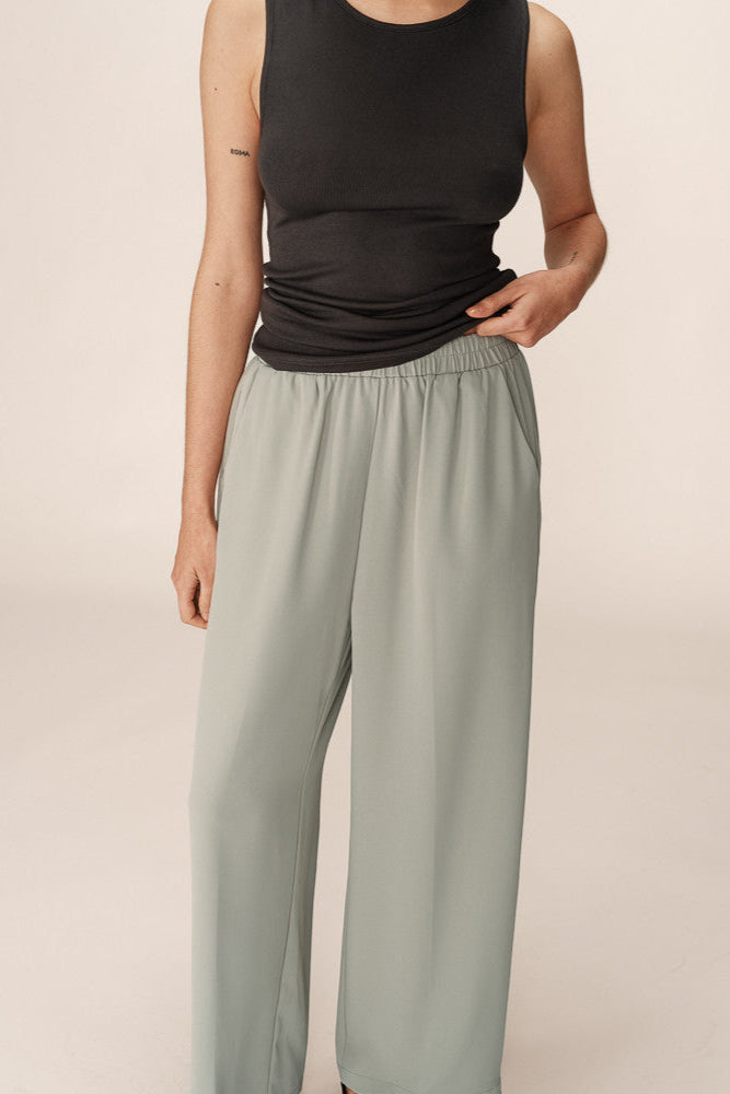 Person wearing a black sleeveless top and light gray pants on a beige background