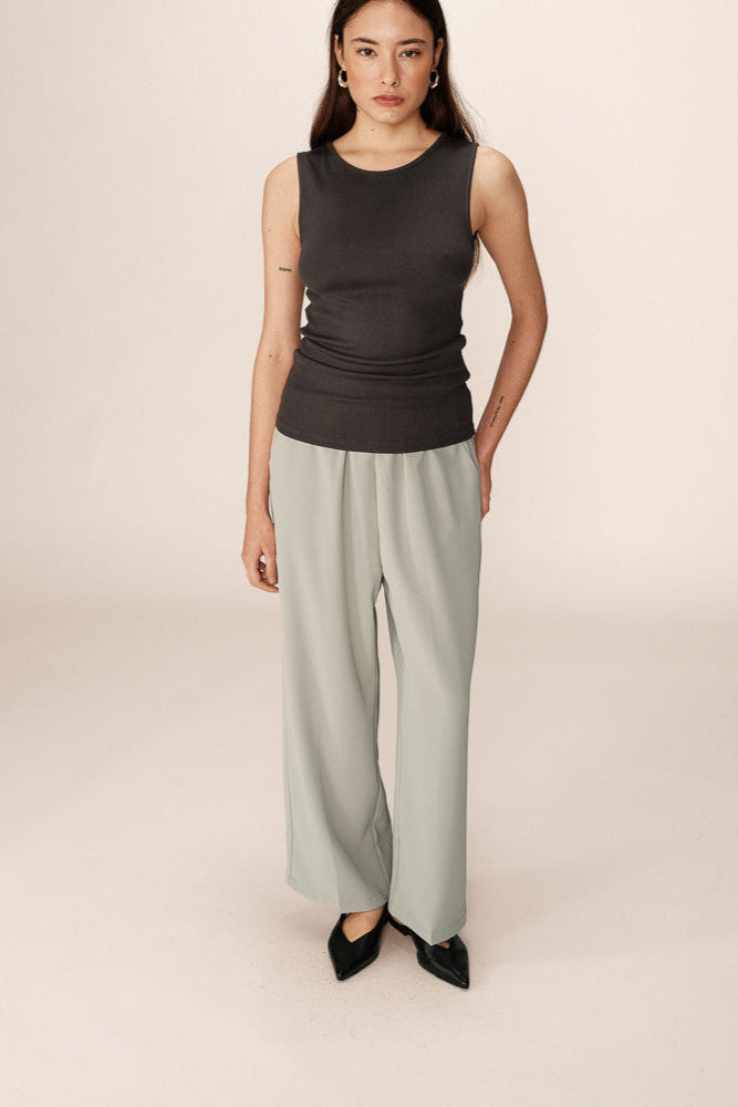 Woman wearing a black sleeveless top and light green wide-leg pants on a beige background