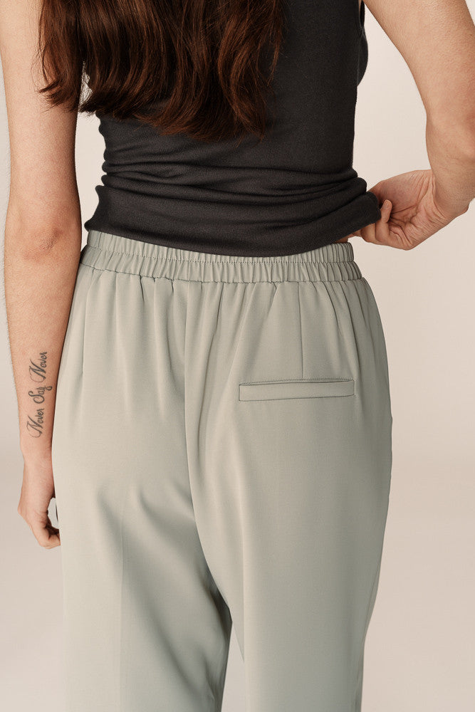 Person wearing a black sleeveless top and light gray pants on a beige background