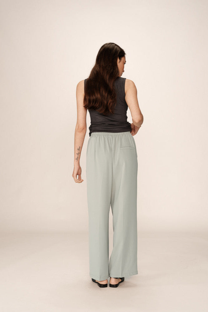 Woman wearing a sleeveless top and light green pants on a plain background