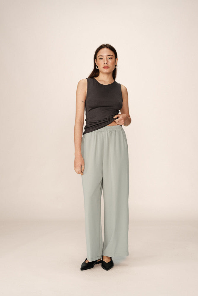 Woman wearing a black sleeveless top and light green wide-leg pants on a beige background